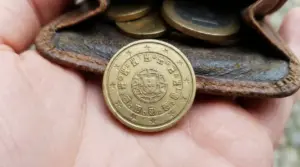 Moneta da 10 centesimi Portogallo 2002 in primo piano su una mano, davanti a un portamonete con altre monete