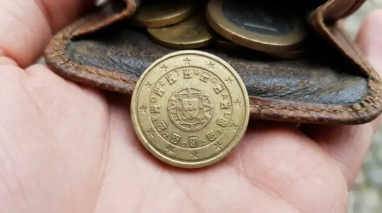 Moneta da 10 centesimi Portogallo 2002 in primo piano su una mano, davanti a un portamonete con altre monete