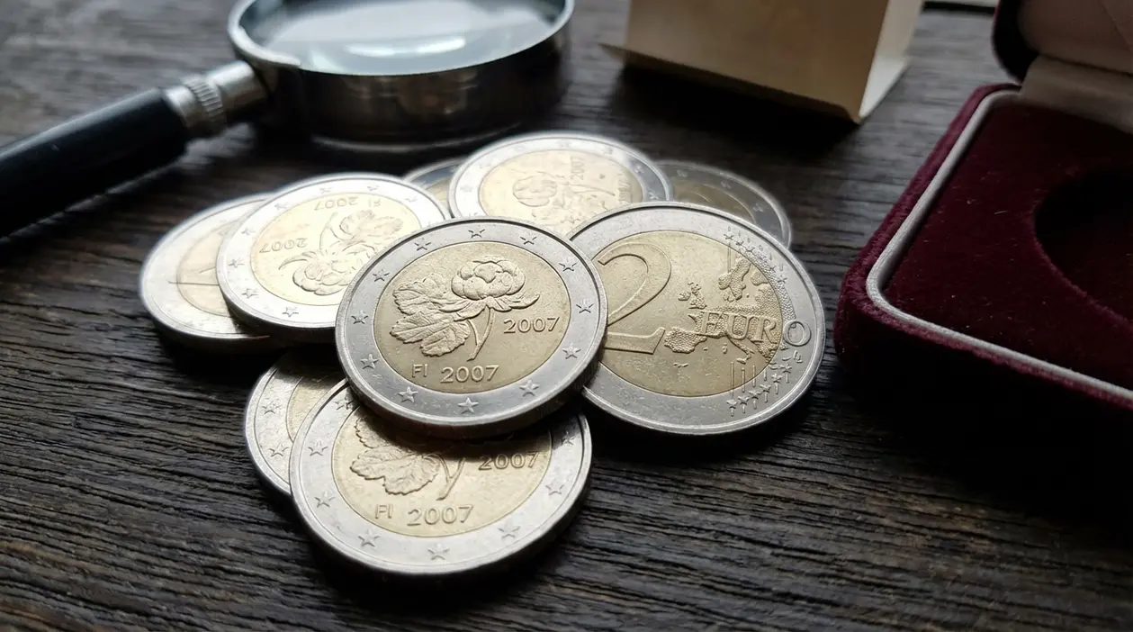 Monete da 2 euro Finlandia 2007 commemorative su tavolo in legno con lente d’ingrandimento e cofanetto