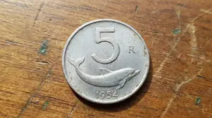 Moneta italiana da 5 lire del 1954 con delfino, appoggiata su una superficie di legno