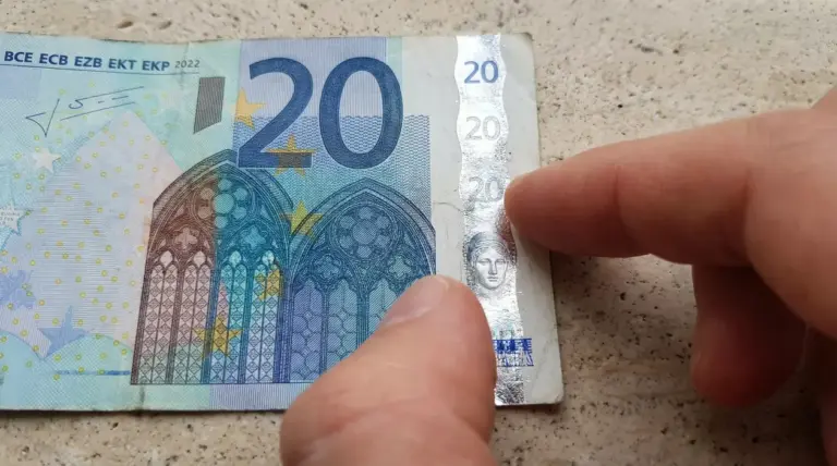 Dettaglio di una banconota da 20 euro con dito che indica la striscia olografica di sicurezza