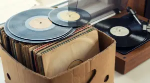 Scatola di cartone con dischi in vinile e un giradischi sullo sfondo, per valutare dischi in vinile rari