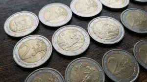 Monete da 2 euro, incluse alcune commemorative, disposte su un tavolo di legno