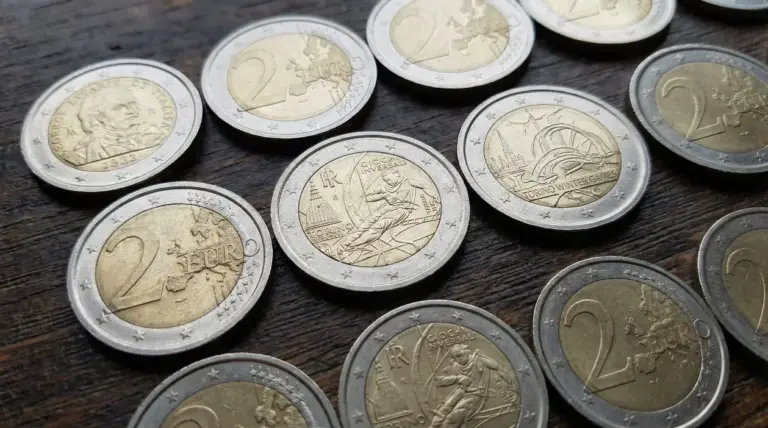 Monete da 2 euro, incluse alcune commemorative, disposte su un tavolo di legno