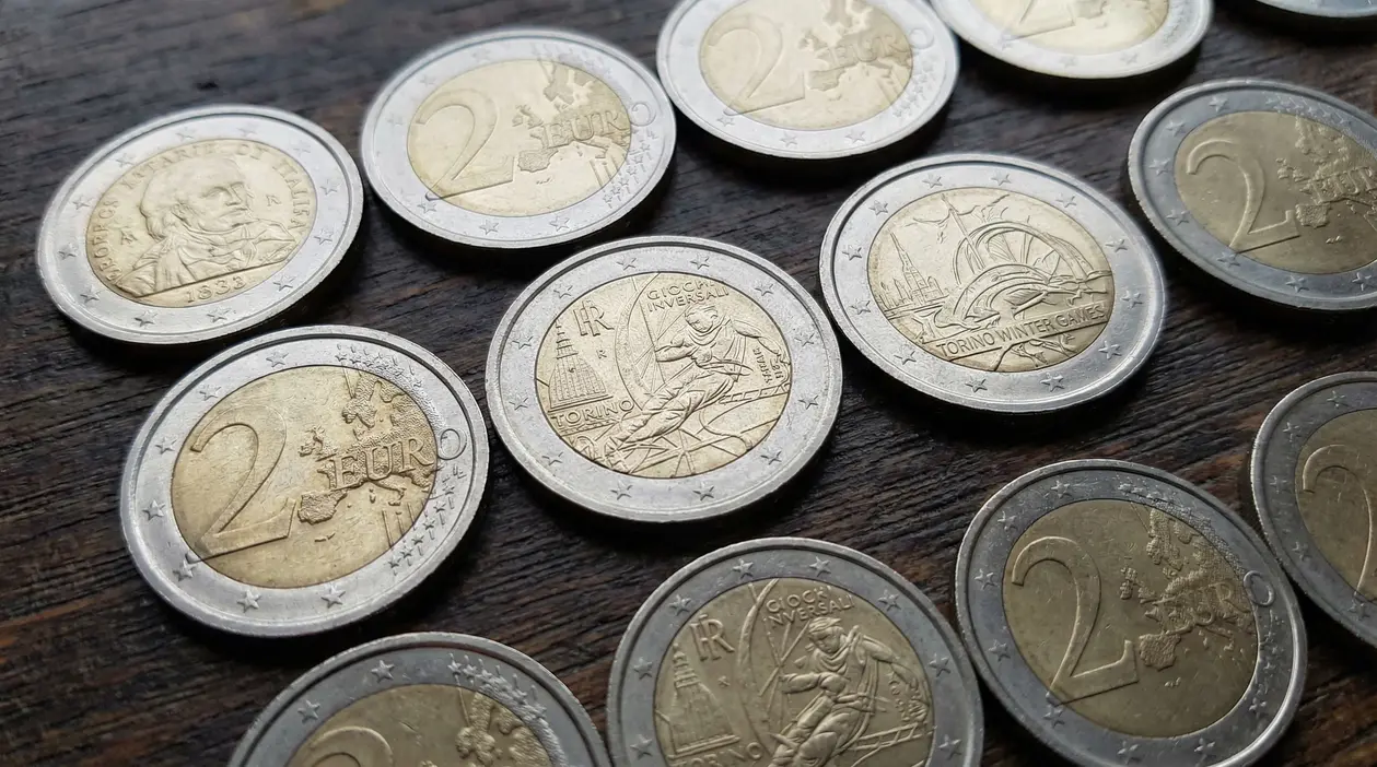 Monete da 2 euro, incluse alcune commemorative, disposte su un tavolo di legno