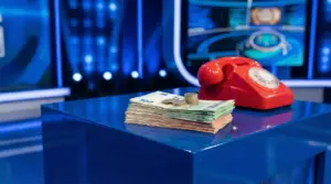 Mazzetta di banconote e monete su un podio in studio TV accanto a un telefono rosso