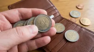 Mano che mostra una moneta da 2 euro commemorativa accanto a un portafoglio con altre monete su un tavolo