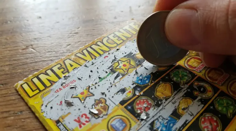 Mano che gratta un biglietto gratta e vinci con una moneta, con simboli di gioco visibili sul tavolo