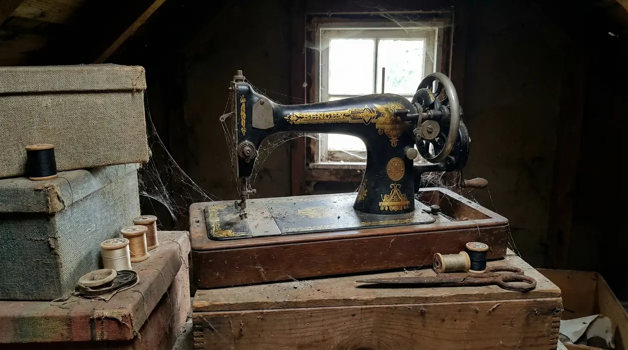 Macchina da cucire d’epoca impolverata in soffitta, con rocchetti di filo e forbici su un tavolo in legno