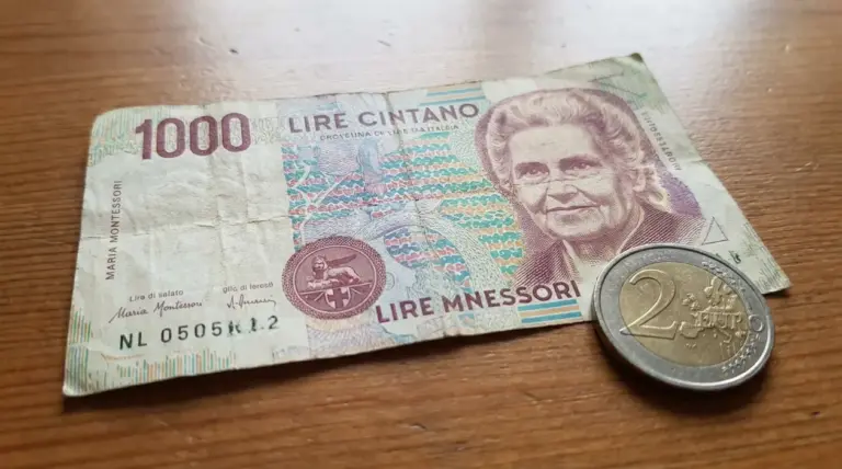 Banconota da 1000 lire Montessori usata su un tavolo di legno, con una moneta da 2 euro accanto