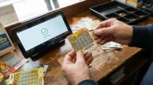 Mani che controllano un gratta e vinci con una moneta vicino a un terminale di verifica in tabaccheria